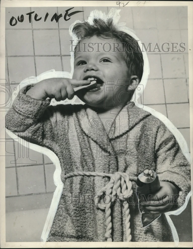 1952 Press Photo Child in bathrobe brushing teeth and holding tube of toothpaste