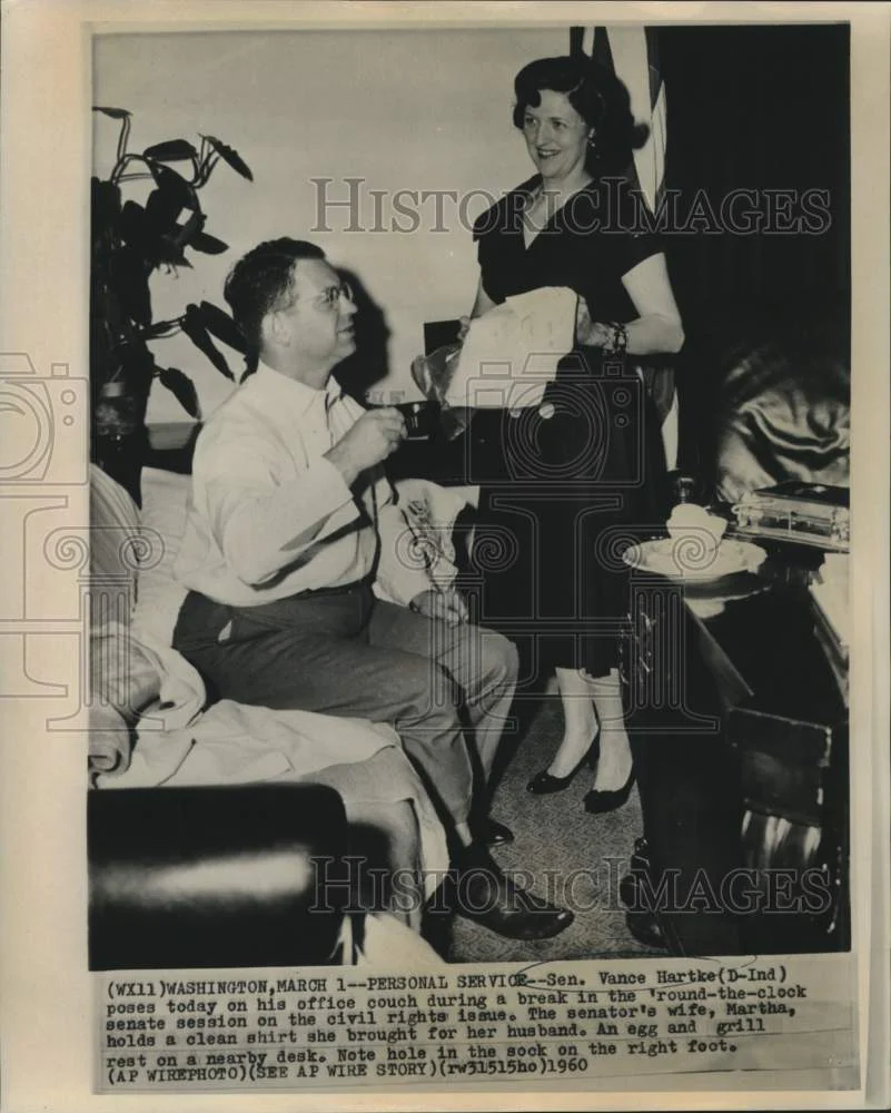 1960 Press Photo Senator Hartke rests on office couch as wife brings clean shirt